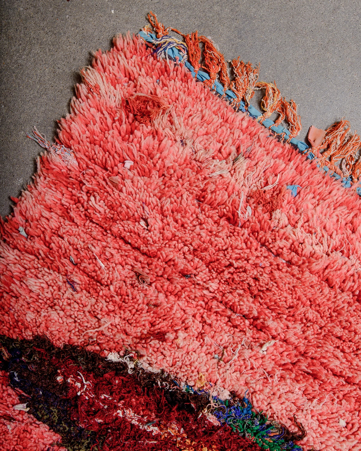 Detail of Berberlin Vintage Berber Rug in shades of red, pink, navy, khaki, burgundy on concrete floor.